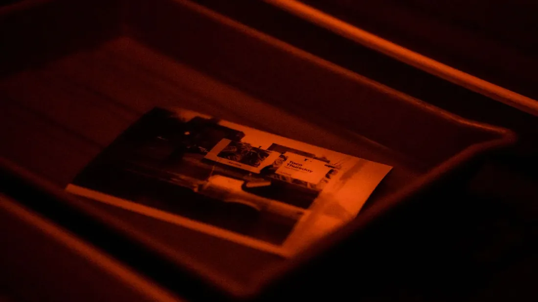 Fotografický papír ve vyvolávací misce pod červeným světlem temné komory, obraz se postupně objevuje